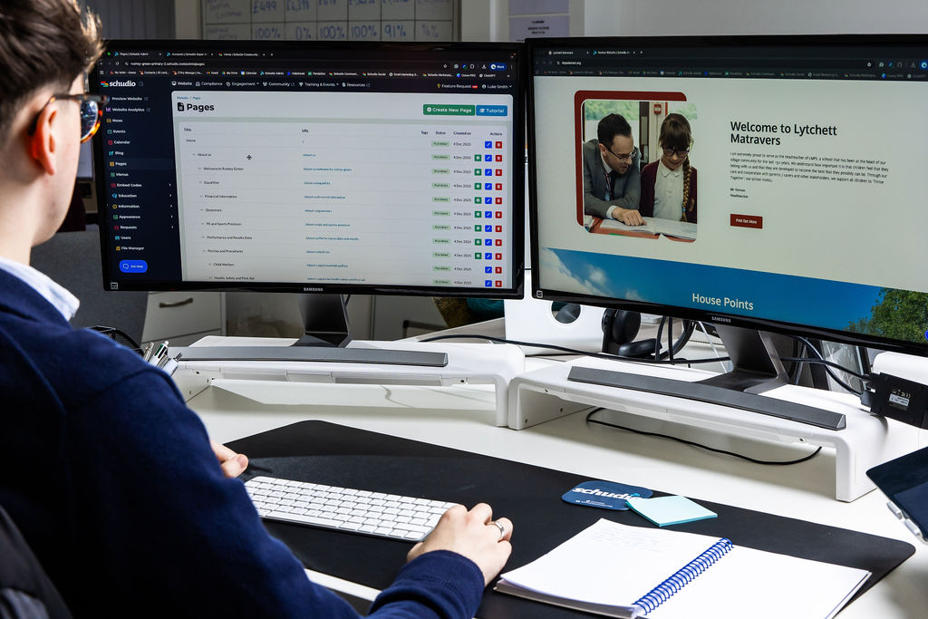 A Schudio team member working across two screens, with the Schudio CMS admin on one and a live primary school website on the other