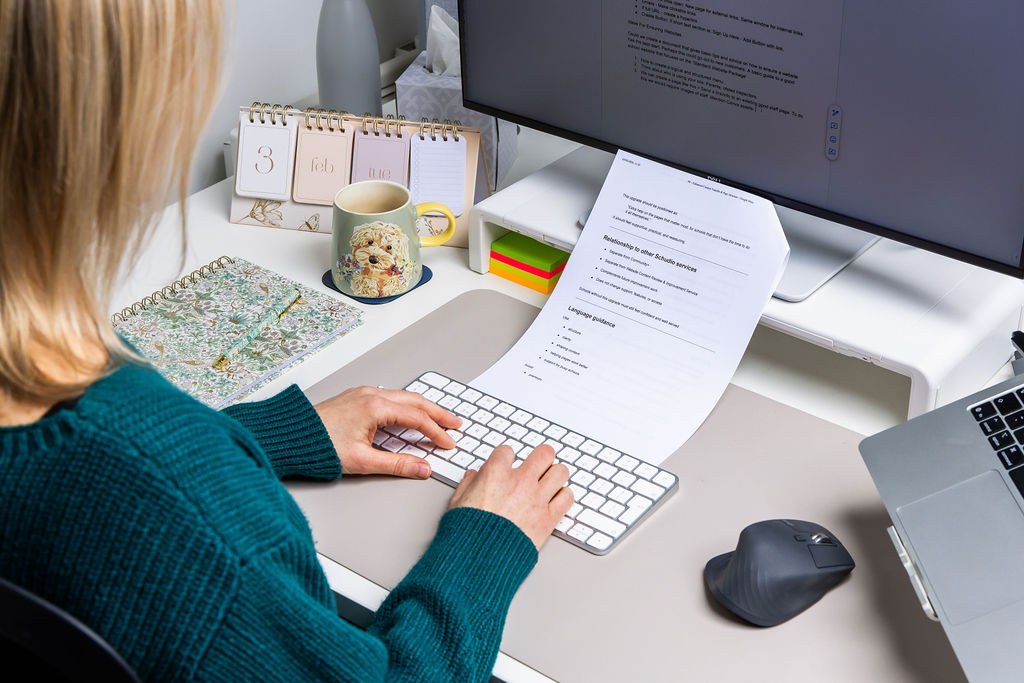 A member of the Schudio team at a screen working through a printed school website compliance checklist