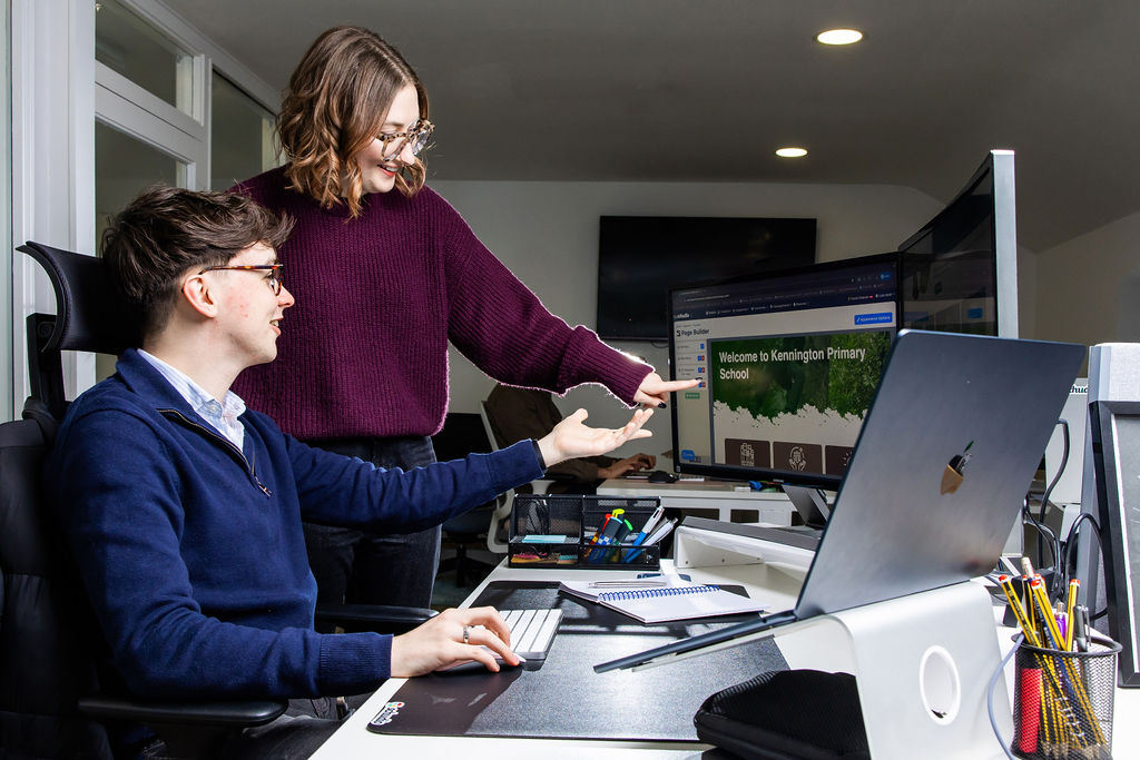 Two members of the Schudio team looking at a primary school website homepage on a monitor in the Schudio office
