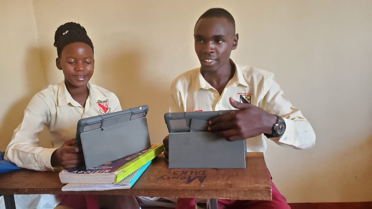 Two Kingstone students in school uniform working on iPads at a classroom desk alongside their history textbook