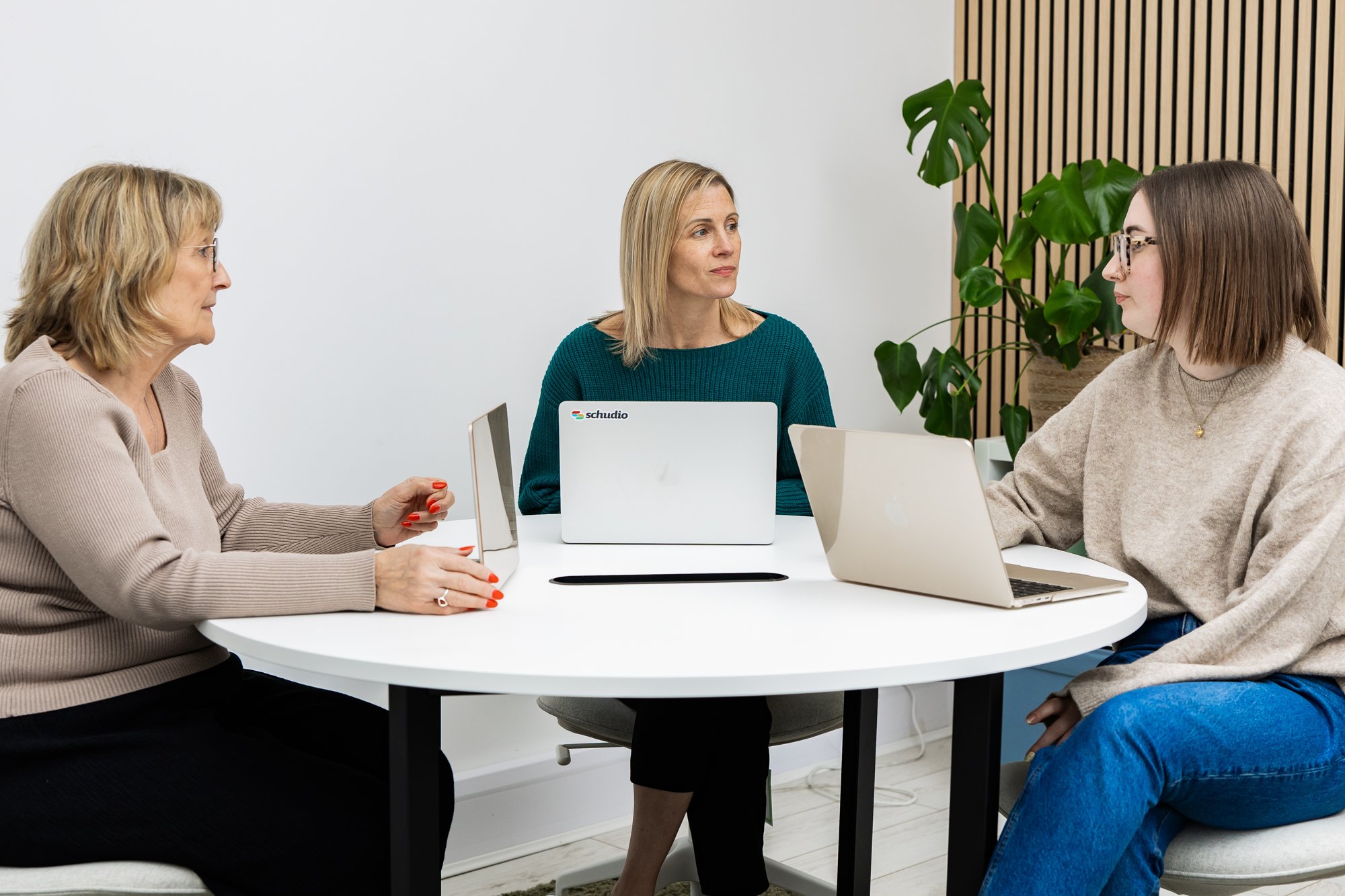 Three members of the Schudio team talking round a table with laptops while planning a school website