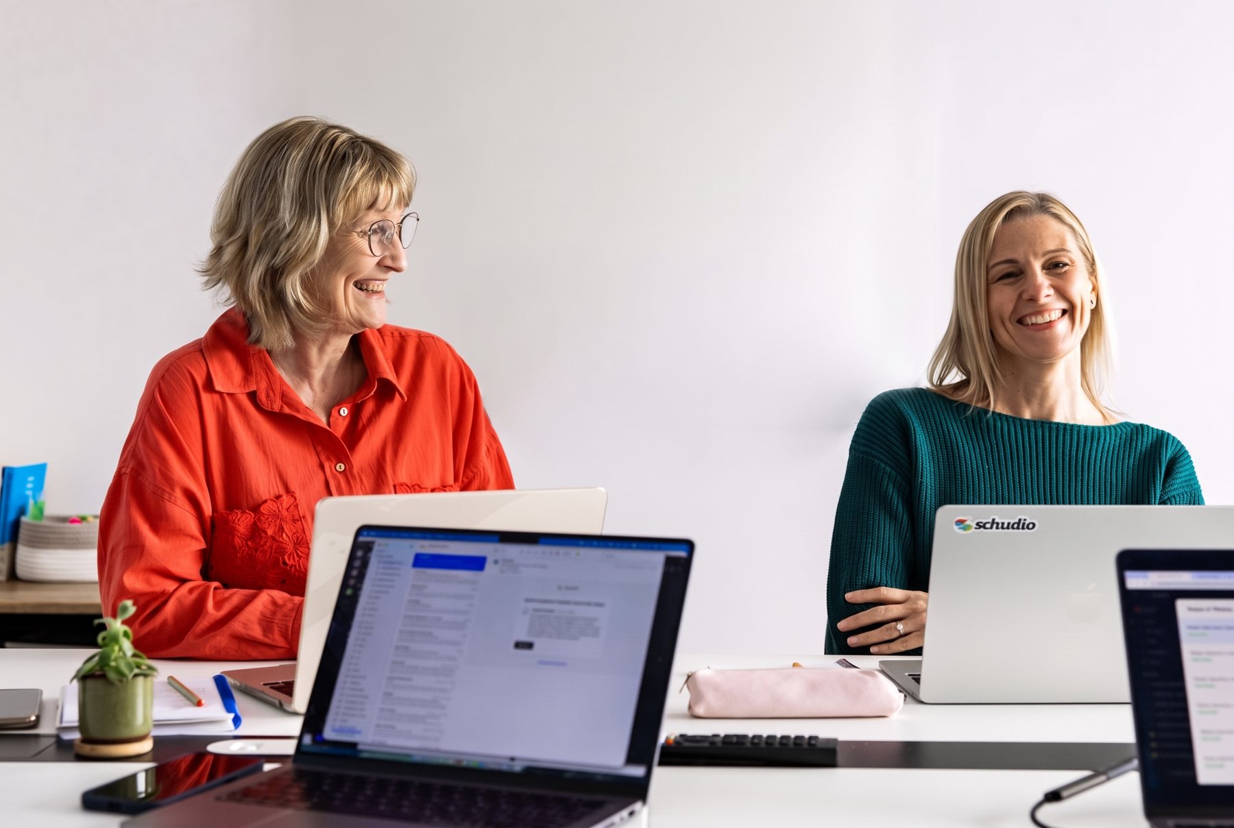 Two members of the Schudio team smiling at their laptops