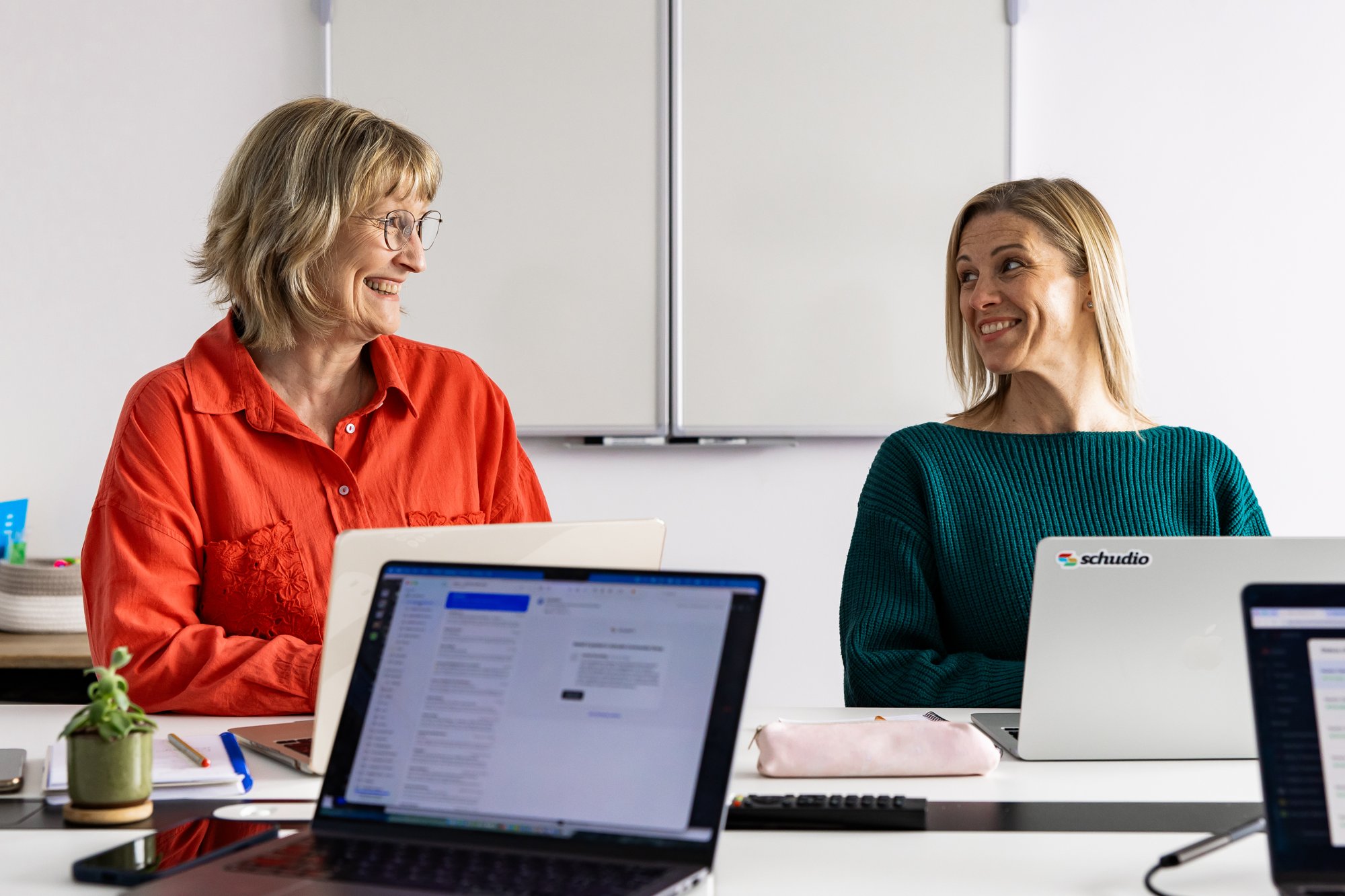 Two Schudio team members smiling at each other across a desk with laptops open