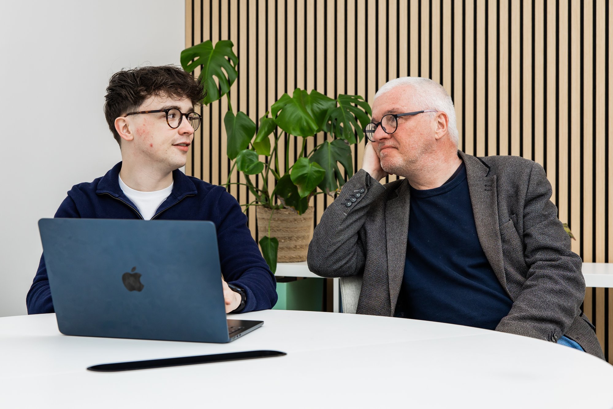 Two Schudio team members talking through a school website on a laptop at a round meeting table