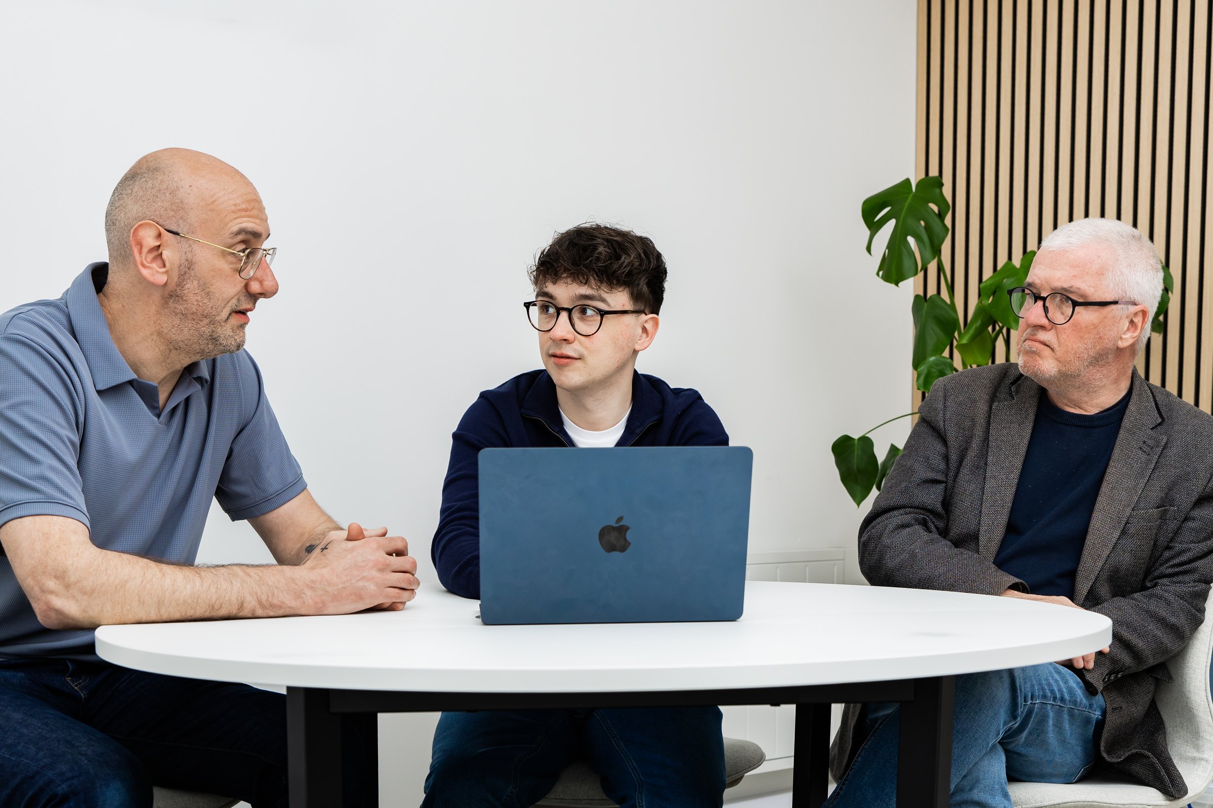 Three members of the Schudio team round a table with a laptop, talking through support for a school website